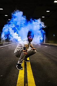 man sitting while holding smoke dispenser at the middle of concrete road thumbnail