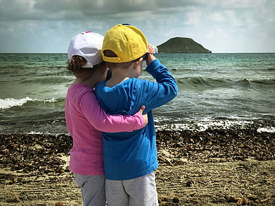 girl wearing pink long-sleeved shirt in front of boy wearing blue long-sleeved shirt standing in front of seashore thumbnail