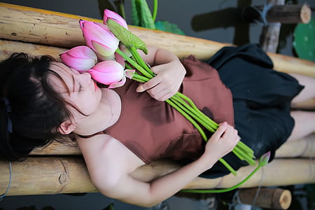 woman holding pink petaled flowers while lying on bamboo thumbnail