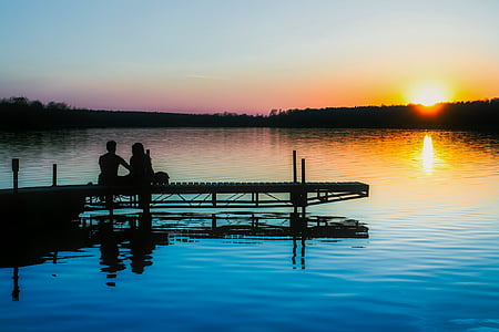silhouette of two people sitting on docks near body of water thumbnail