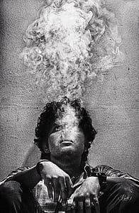 grayscale photo of man leaning on wall while smoking thumbnail