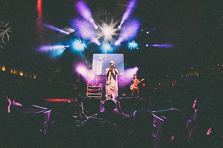 low-light photo of man performing on stage with assorted-color strobe lights surrounded by group of people thumbnail