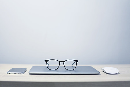 black framed eyeglasses on MacBook Air beside Apple Magic Mouse and silver Android smartphone thumbnail