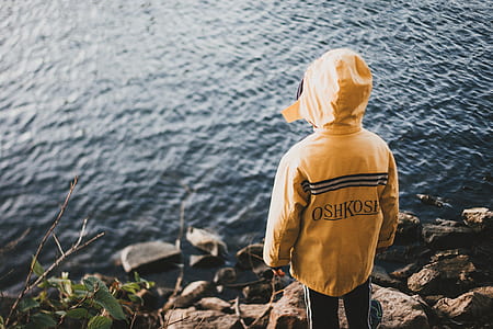 boy wearing yellow hoodie facing body of water thumbnail