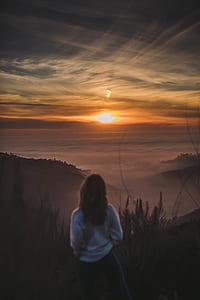 woman standing on mountain peak facing sunset thumbnail