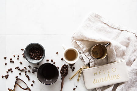 flat-lay photography of coffee seeds bowl, three empty mugs, white Hello Sunshine coin purse, and spoon of coffee seeds on table thumbnail