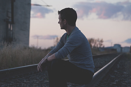 man wearing blue sweatshirt sitting on silver train way thumbnail