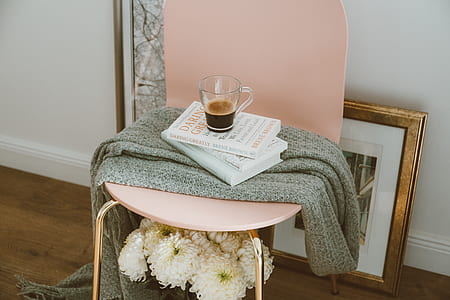 pink chair with gray scarf over books and clear glass mug thumbnail
