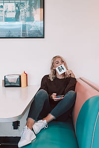 woman sitting on brown and green leather sofa while holding pink phone and white card with 84 print thumbnail