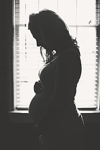 grayscale photography of pregnant woman near window thumbnail