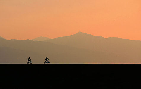 two person riding on bicycle on black surface during golden hour thumbnail