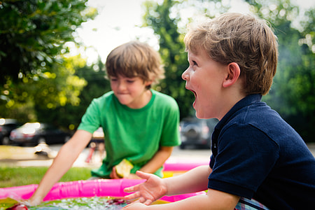 two boy wearing green and blue t-shirts playing outside near green leaf trees at daytime thumbnail