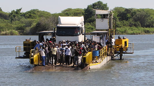 mass of people standing on barge near green mountains thumbnail