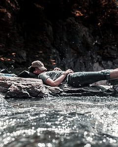 man laying on stone surrounded by body of water during daytime thumbnail