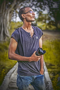 Shallow Focus Photography of Man Wearing Gray T-shirt Holding Dslr Camera Lens thumbnail