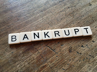 white bankrupt scrabble tiles on brown wooden surface thumbnail