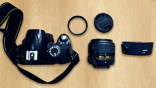 black Nikon DSLR camera beside lens on brown wooden surface thumbnail