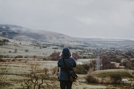 selective focus photography of person in hooded jacket looking at trees and mountains thumbnail