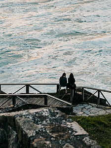 two person sitting front of body of water thumbnail
