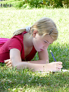 girl laying on grass field while writing on lined paper thumbnail