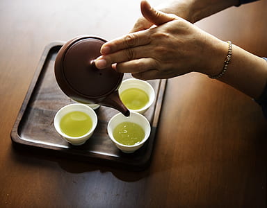 person holding brown teapot pouring tea on white teacups thumbnail