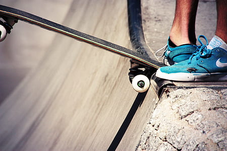 close-up photography of person wearing blue Nike low-top sneakers stepping on black skateboard on ramp during daytime thumbnail