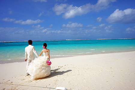 photography of couple wearing white wedding dress and suit standing on beige sand near sea under gray and blue sky during daytime thumbnail