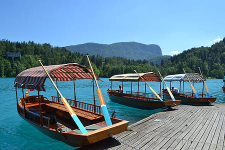 three brown wooden boats on body of water near mountain range thumbnail