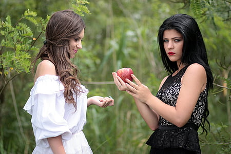 two women in black and red dresses near green trees at daytime thumbnail