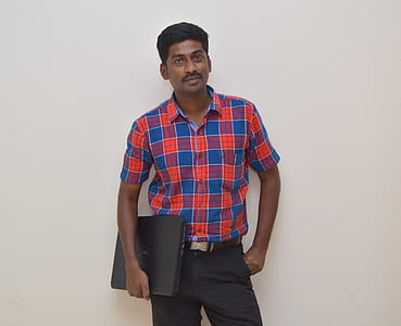 man holding black laptop computer while standing near white painted wall thumbnail