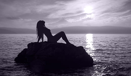 silhouette photography of woman sitting on rock formation near body of water thumbnail