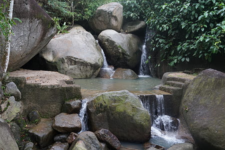 waterfalls surrounded by large rocks and plants thumbnail
