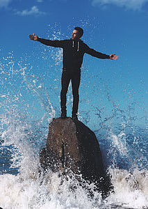 man standing on stone surrounded by water during daytime thumbnail