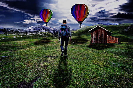 man walking on green grass field under two hot air balloons thumbnail