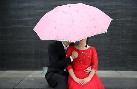 man hugging woman wearing red long-sleeved dress under umbrella thumbnail