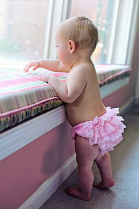 baby in pink ruffle underwear standing in front of bed thumbnail