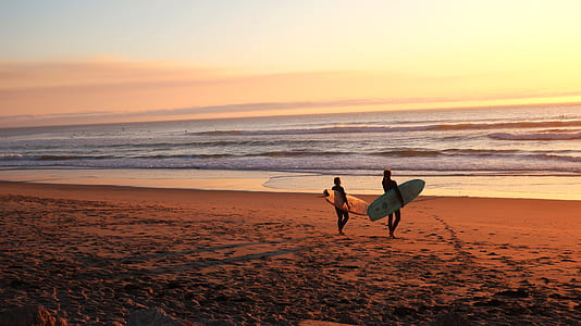 two people carrying surfboard near shoreline thumbnail