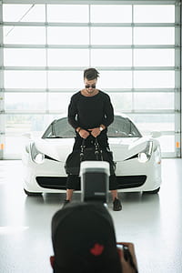 man holding duffle bag and standing on front of white Ferrari 458 Italia near window thumbnail
