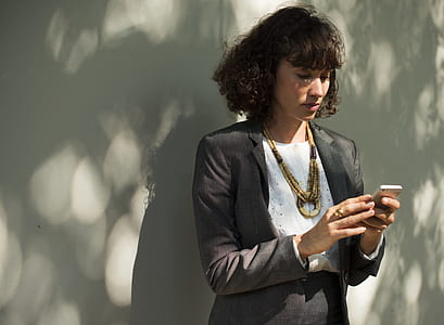 woman holding phone while standing beside wall thumbnail