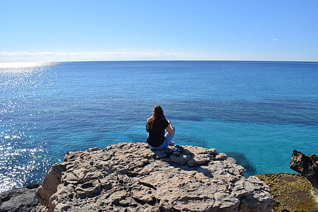 person sitting on mountain cliff facing sea thumbnail