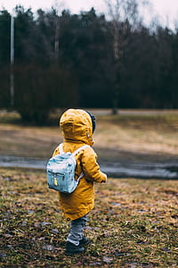 child wearing yellow hoodie and blue backpack walking on grass field thumbnail