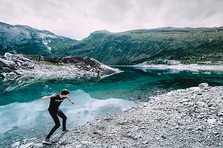 man throwing stones in lake during daytime thumbnail