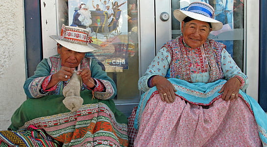 two woman in pink and green long-sleeved dresses sitting near white door thumbnail