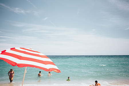 A beach umbrella with people swimming in the background thumbnail