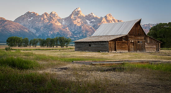 brown wooden barn near trees and brown mountains thumbnail