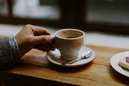 person holding white ceramic mug, saucer and spoon thumbnail