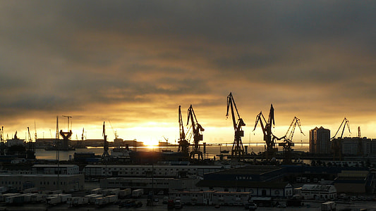 silhouettes of cranes above building under cloudy sky thumbnail