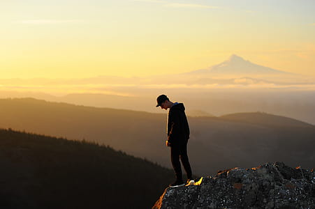 man standing on cliff near mountain range under golden hour thumbnail