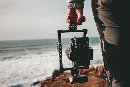 selective focus photography of person holding camera with gimbal facing sea thumbnail