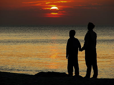 silhouette of two people standing near seashore at sunset thumbnail